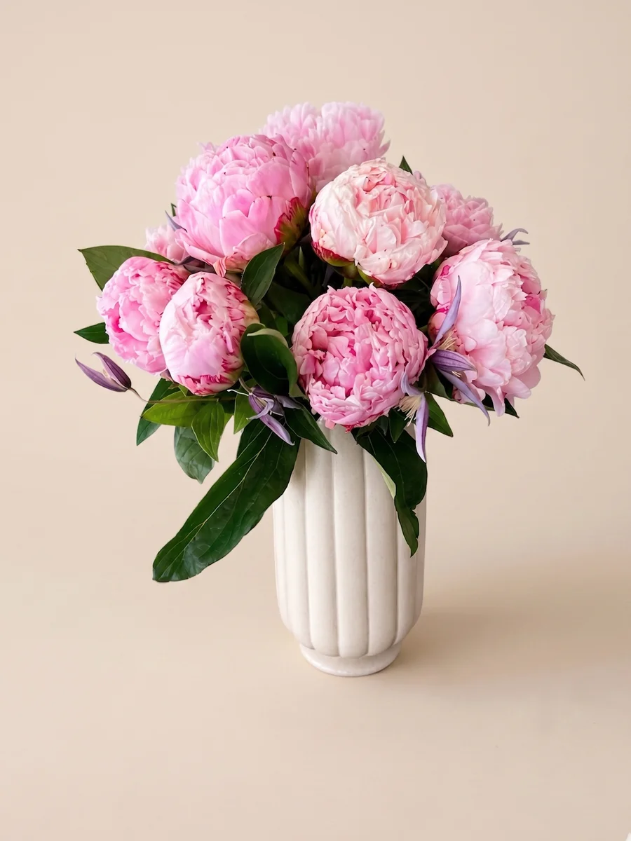 The Penelope - lush pink peonies with purple clematis in a tall white ribbed vase